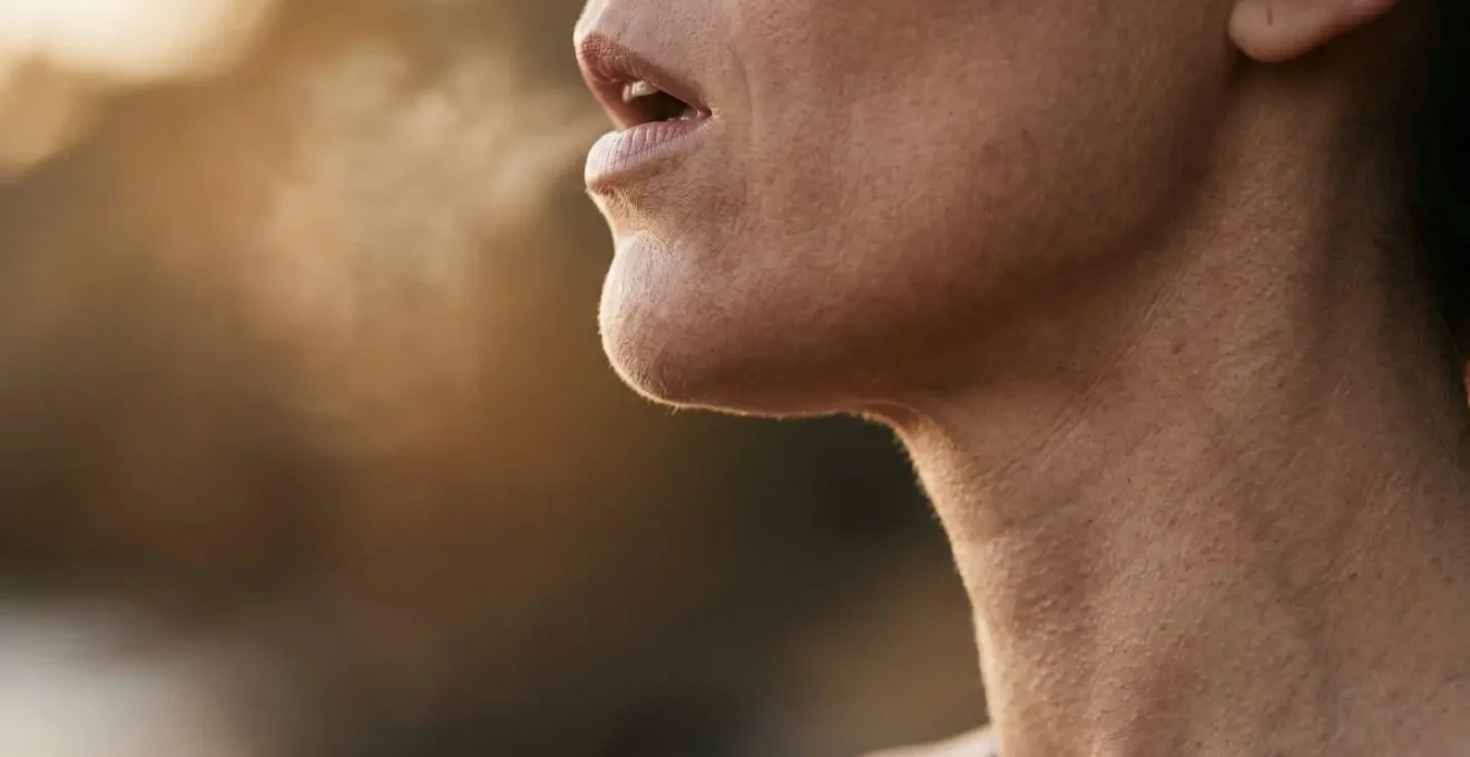 Macro photograph showing a person's throat and jaw in profile during vocal toning practice, capturing the physical vibration and resonance of sound through the body